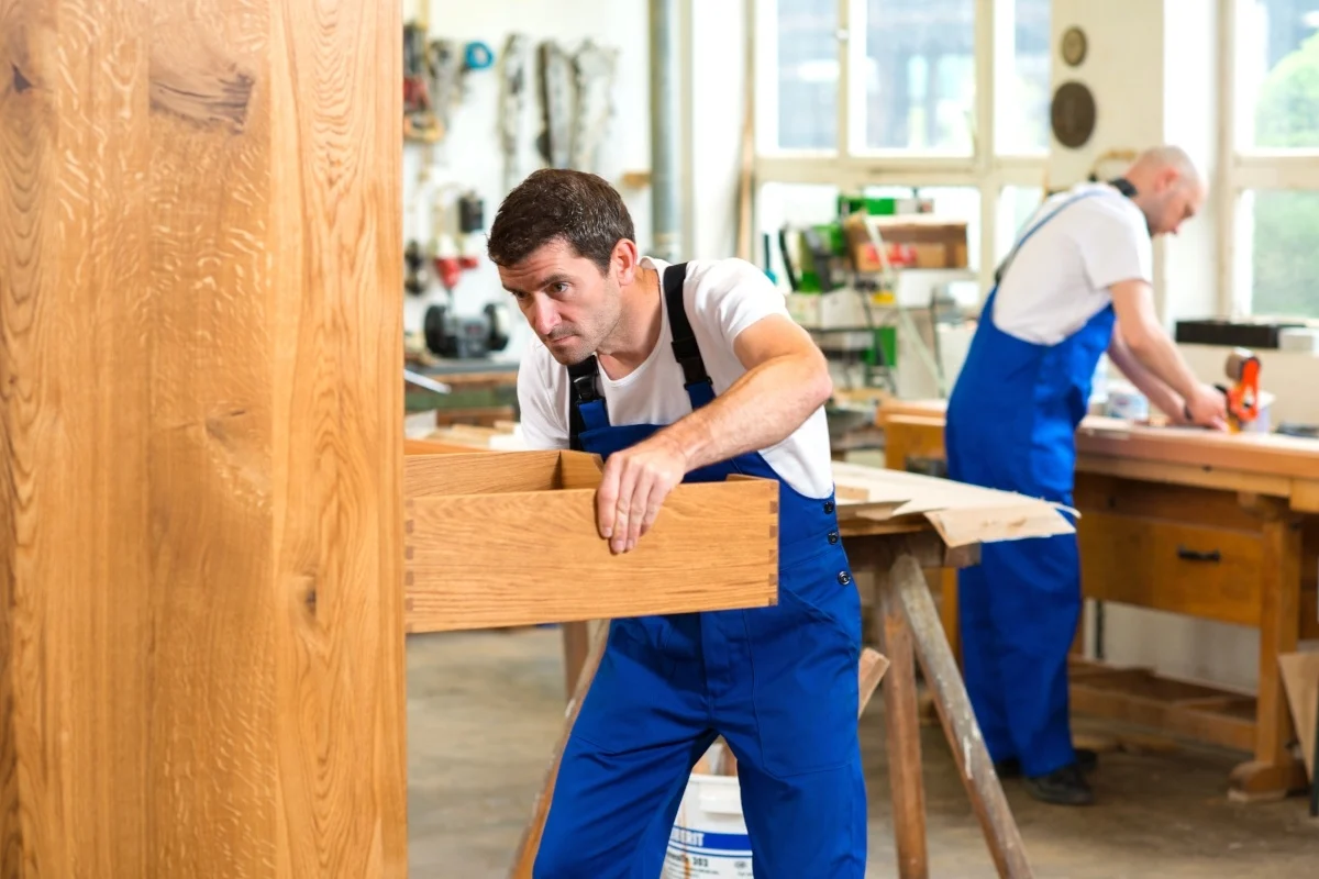 a-person-in-blue-overalls-holding-a-piece-of-wood